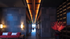 Un hall d’entrée moderne avec un canapé rouge, un banc en bois, une plante en pot et un couloir menant à un espace lumineux.