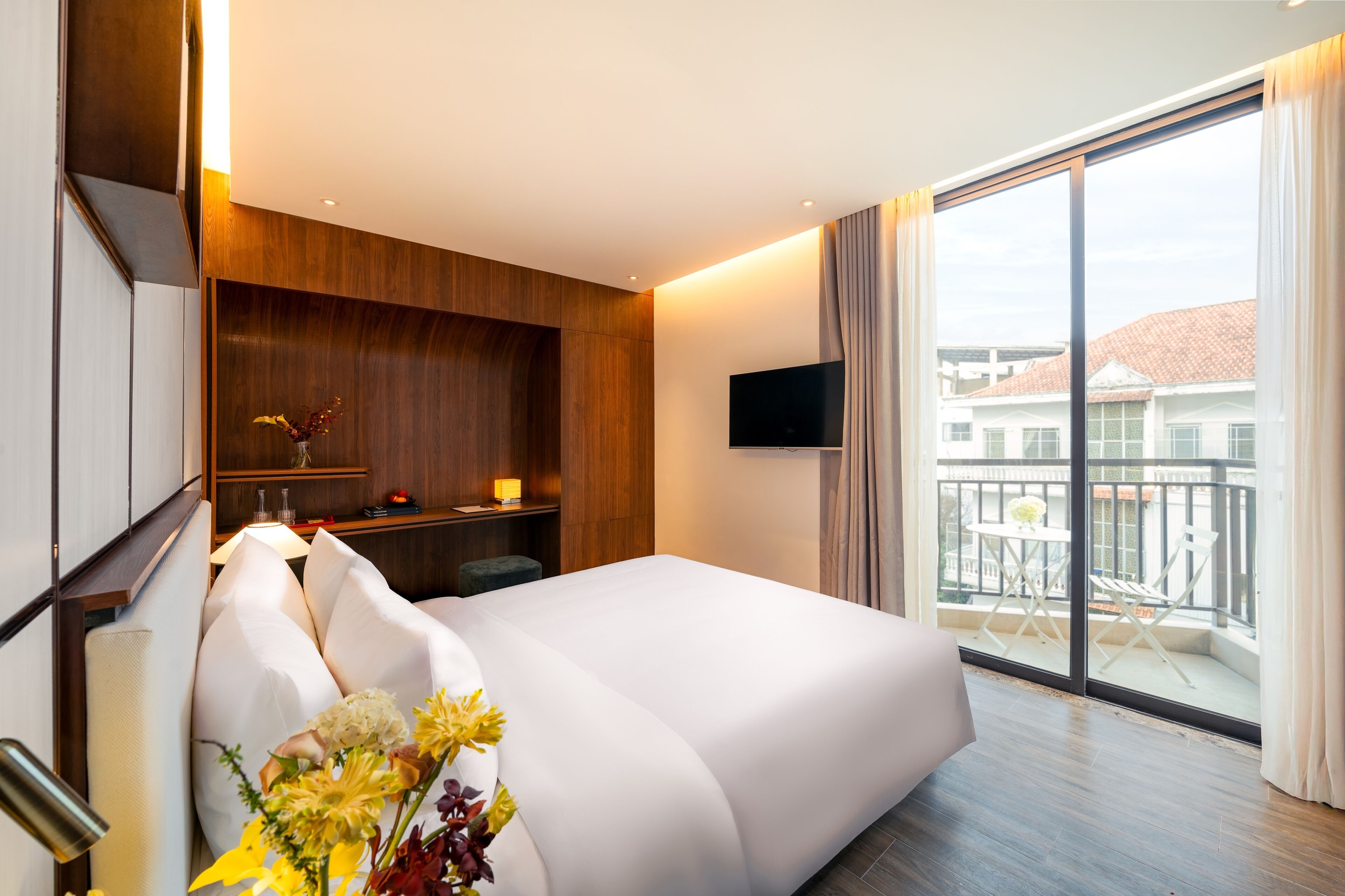 Une chambre d’hôtel moderne dotée d’un grand lit, d’un bureau avec une lampe, d’une télévision à écran plat et d’un balcon offrant une vue sur les bâtiments.