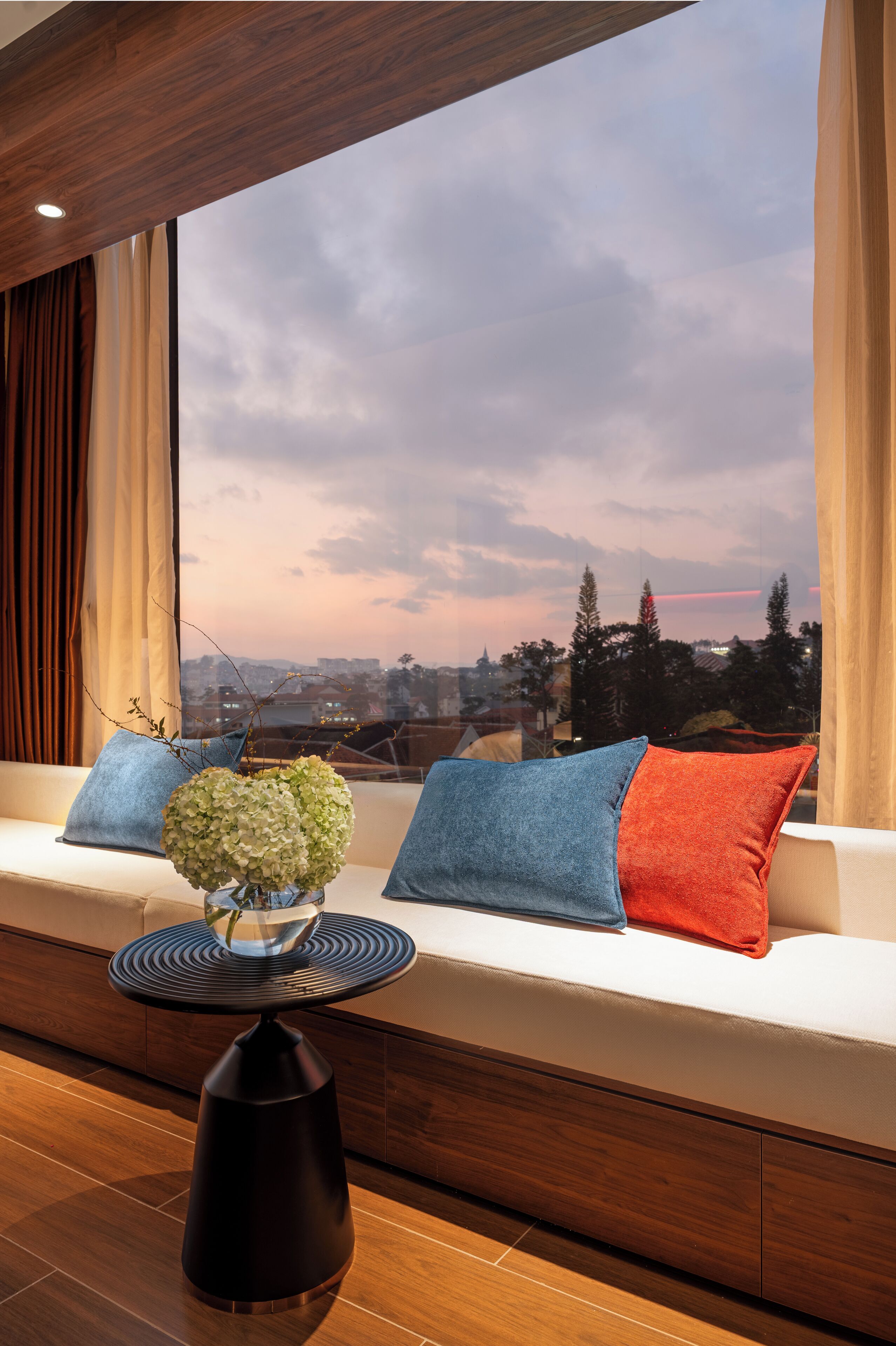 A modern living room with a sofa, a round table, and a view of a cityscape through large windows.