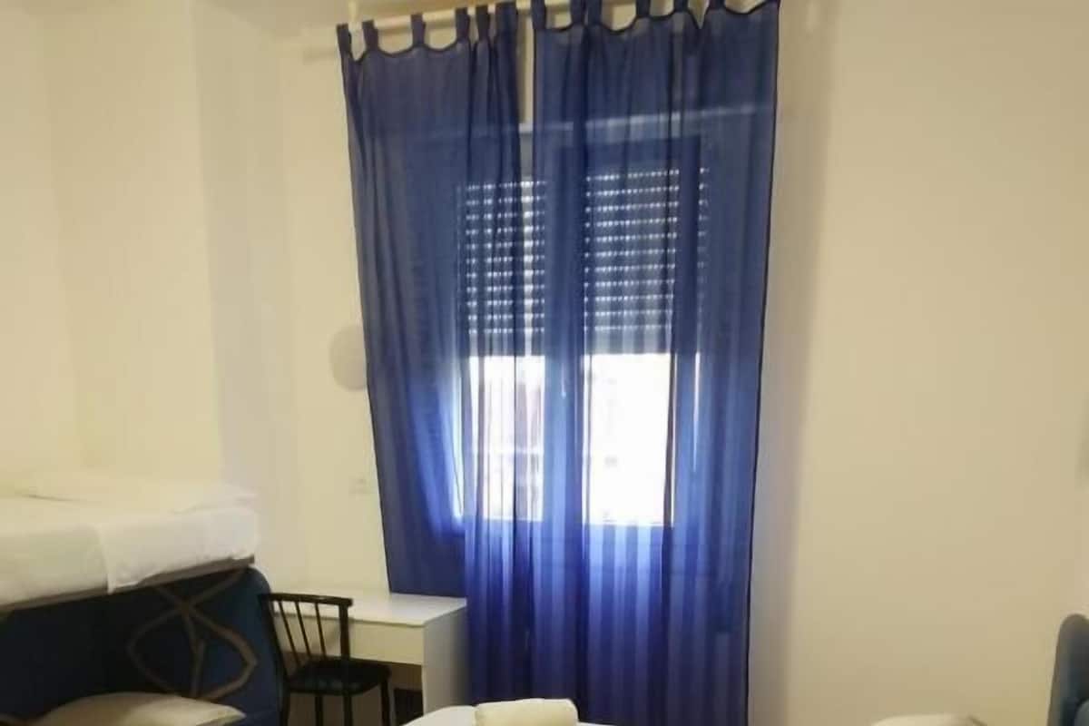 A hotel room with a bed, a desk, a chair, and a window with curtains.