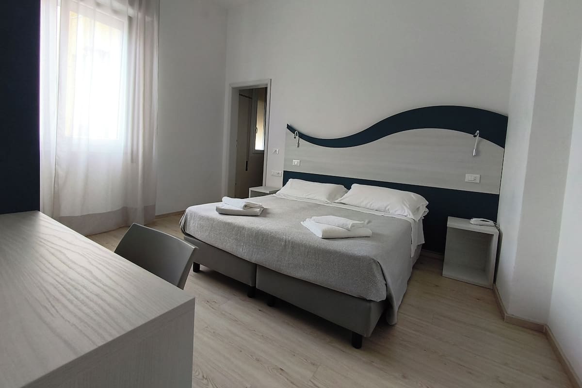 A modern hotel room with a bed, bedside tables, a desk, and a view of the outdoors.