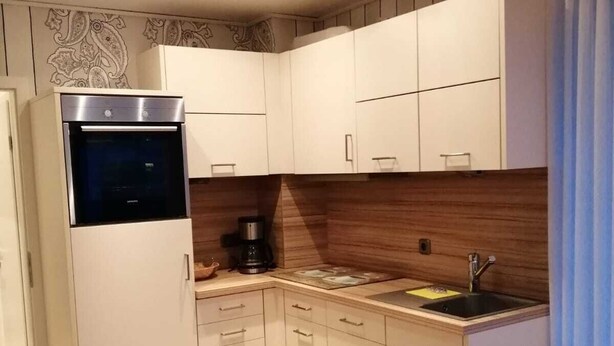 Eine kleine Küche mit weißen Schränken, einem Backofen, einer Kaffeemaschine und einem Sp ülbecken.