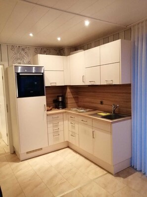 A compact kitchen with white cabinets, a built-in oven, a coffee maker, and a sink. - Prinzenhof Vacation Apartment with Ocean View, Balcony, and Beach Chair Included (Grömitz)