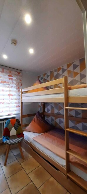 A bunk bed room with a patterned wall, a chair, and a radiator. - Prinzenhof Vacation Apartment with Ocean View, Balcony, and Beach Chair Included (Grömitz)