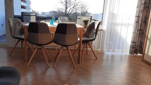 Ein Essbereich mit einem Holztisch, vier Stühlen, einem Fenster mit Vorhängen und Blick auf Gebäude.