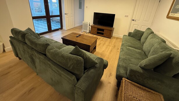 A living room with two green sofas, a wooden coffee table, and a TV on a stand. - The Elements Residence (Chepstow)