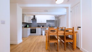 A modern kitchen with white cabinetry, a wooden dining table, and a built-in oven. - The Elements Residence (Chepstow)
