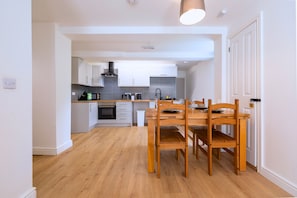 A modern kitchen with white cabinetry, a wooden dining table, and a built-in oven.