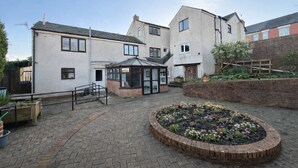 A courtyard with a brick pathway, a conservatory, and a flower bed. - The Elements Residence (Chepstow)