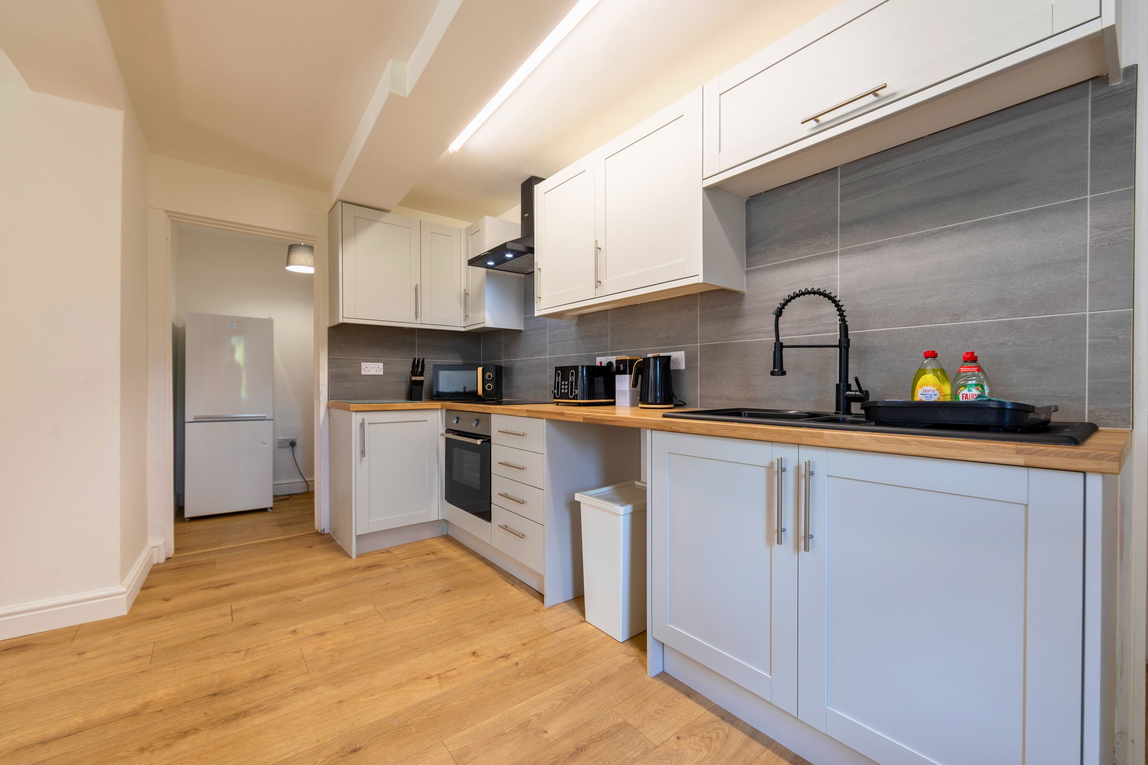 A modern kitchen with white cabinets, a stainless steel refrigerator, and a wooden countertop.