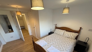 A bedroom with a wooden bed, patterned bedding, two bedside tables, a nightstand, and a hanging lamp. - The Elements Residence (Chepstow)