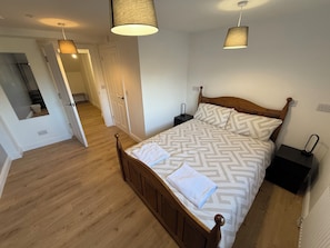 A bedroom with a wooden bed, patterned bedding, two bedside tables, a nightstand, and a hanging lamp. - The Elements Residence (Chepstow)