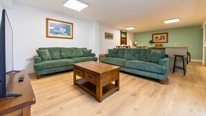 A living room with two green sofas, a wooden coffee table, and a TV stand. - The Elements Residence (Chepstow)