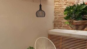 A small, enclosed patio area with a slatted ceiling, a hanging light fixture, a stone planter with a plant, two white chairs, and a patterned tiled floor. - Dimore del Borgo Antico Corte da Lezze Luxury House Venice (Venezia)