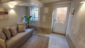A living room with a beige sofa, a rug, a wall-mounted abstract painting, a potted plant, and a door with a window. - Dimore del Borgo Antico Corte da Lezze Luxury House Venice (Venezia)