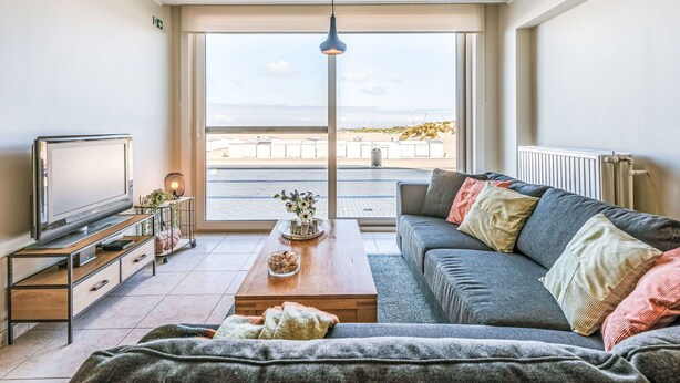A modern living room with a large window, a flat-screen TV, a sofa, a coffee table, and a pendant light. - Nice apartment for 4 guests with WIFI and TV (Bruges)
