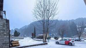 A snowy parking lot with a car and a building with a stone facade. - Cosy apartment for 4 people with WIFI, TV, balcony and pets allowed (Scalcoggia)