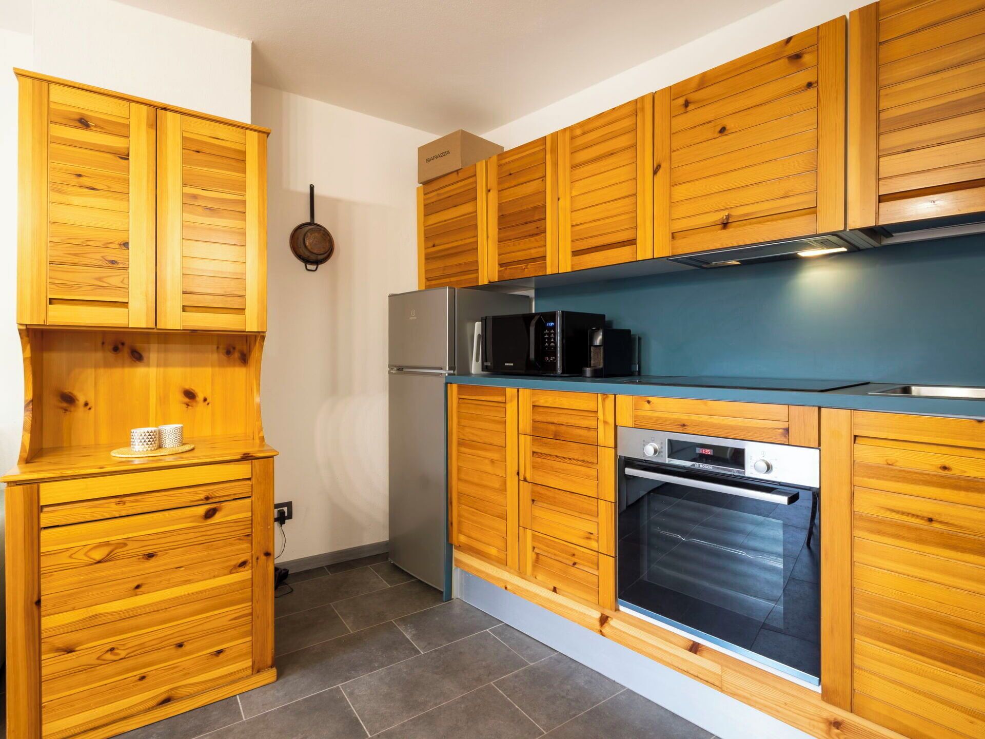 A modern kitchen with wooden cabinetry, a stainless steel refrigerator, a microwave, a coffee maker, and an oven.
