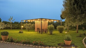 Ein Pavillon mit Lichterketten, umgeben von einem gepflegten Rasen und Blumentöpfen.