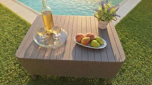 A wooden table with a bottle of wine, three glasses, and a plate of fruit by a pool. - Cosy apartment for 4 guests with A/C, WIFI, private pool, TV and terrace (Posada)