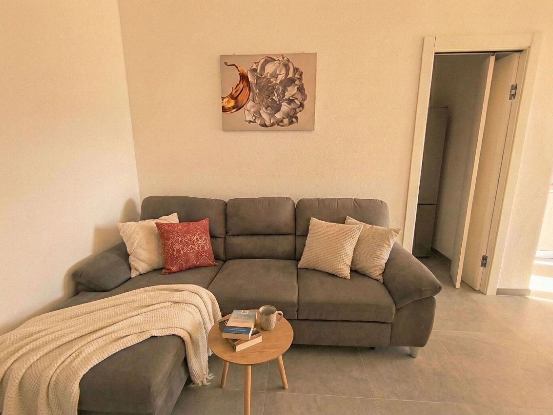 Un salon avec un canapé d’angle gris, une petite table basse ronde en bois et un plaid beige.