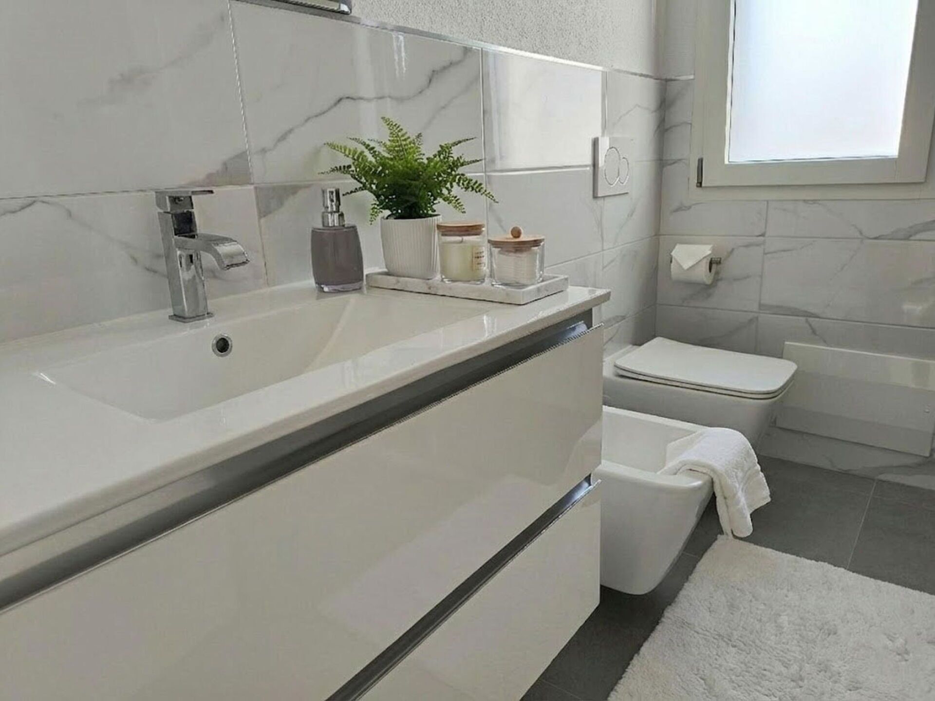 Ein modernes Badezimmer mit einem großen weißen Waschbecken, einem Spiegel, einer Toilette und einer Badewanne.