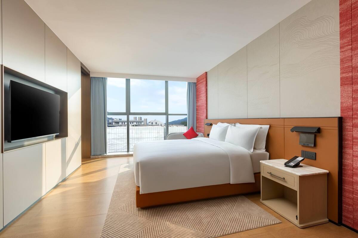 Una habitació d'hotel moderna amb un llit gran, un telèfon a la nit i un televisor fixat a la paret.