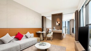 A modern hotel room with a sofa, a coffee table, a TV, a desk, and a chair. - Ramada by Wyndham Zhaoqing Dawang (Zhaoqing)