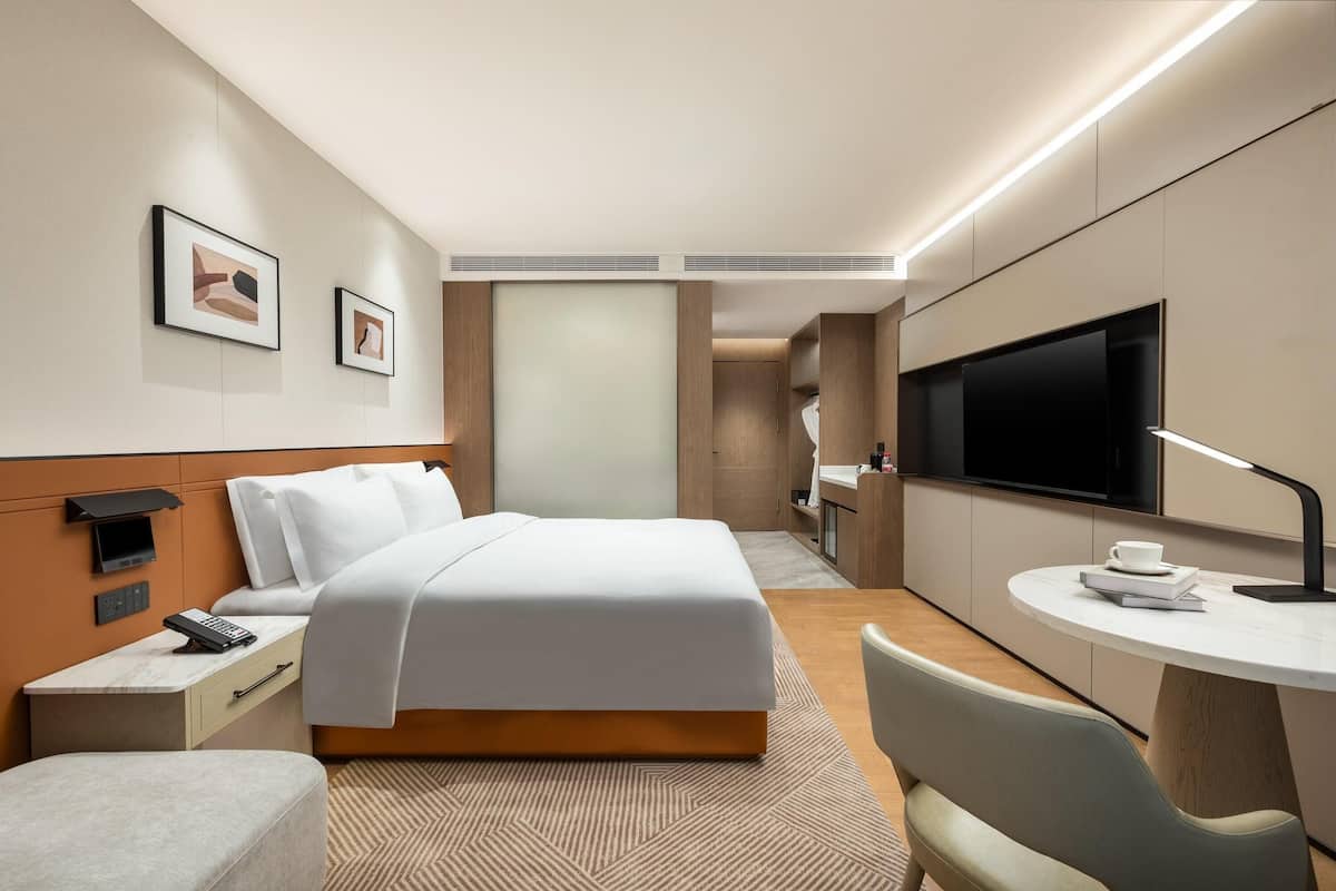 Habitació d'hotel moderna amb llit, taula de nit, televisió i una petita zona de menjador.