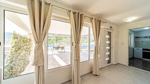 A room with large windows, a view of a patio with outdoor furniture, and a kitchen area. - Apartman Doris by Villas Guide (Vela Luka)