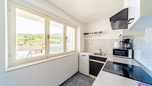 A compact kitchen with a window view, a dishwasher, a microwave, and a coffee maker. - Apartman Doris by Villas Guide (Vela Luka)