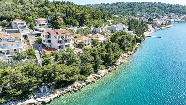 A coastal residential area with houses along a clear blue sea, surrounded by dense greenery. - Apartman Doris by Villas Guide (Vela Luka)