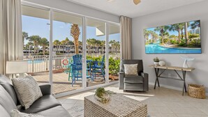 A spacious living room with a large sliding glass door leading to a pool area, a grey sofa, a coffee table, and a ceiling fan. - Gulfside 107 at Destin West ~ Ground Floor  ~ Direct Pool & Beach Access (Fort Walton Beach)