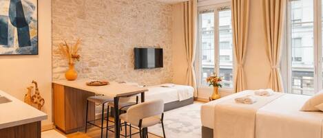 A modern hotel room with a stone wall, a desk with a chair, a bed, and a TV.
