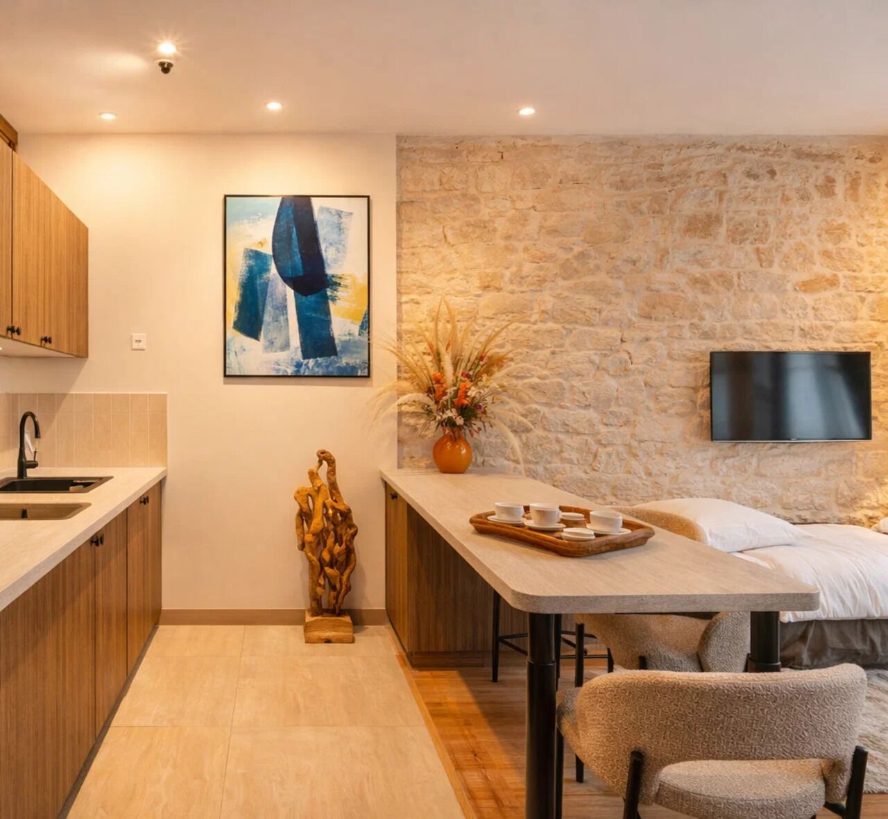 Cuina moderna amb armaris de fusta, paret de pedra, televisor penjat i zona de dinar amb taula i cadires.