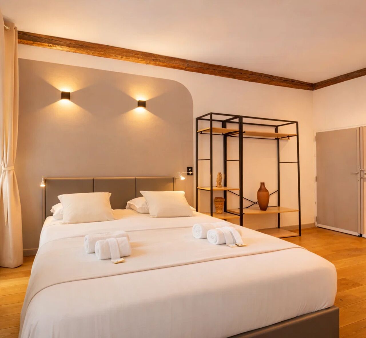 Una habitación de hotel con una cama grande, techo de madera y estante empotrado con objetos decorativos.