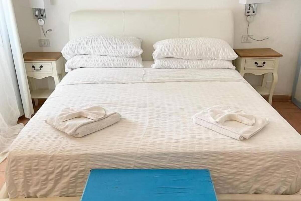 Un lit avec une literie blanche et deux oreillers, une table de chevet bleue et deux tables de nuit avec des lampes.