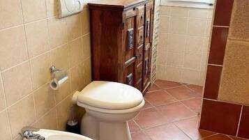 Een badkamer met twee toiletten, een bidet en een kastje.