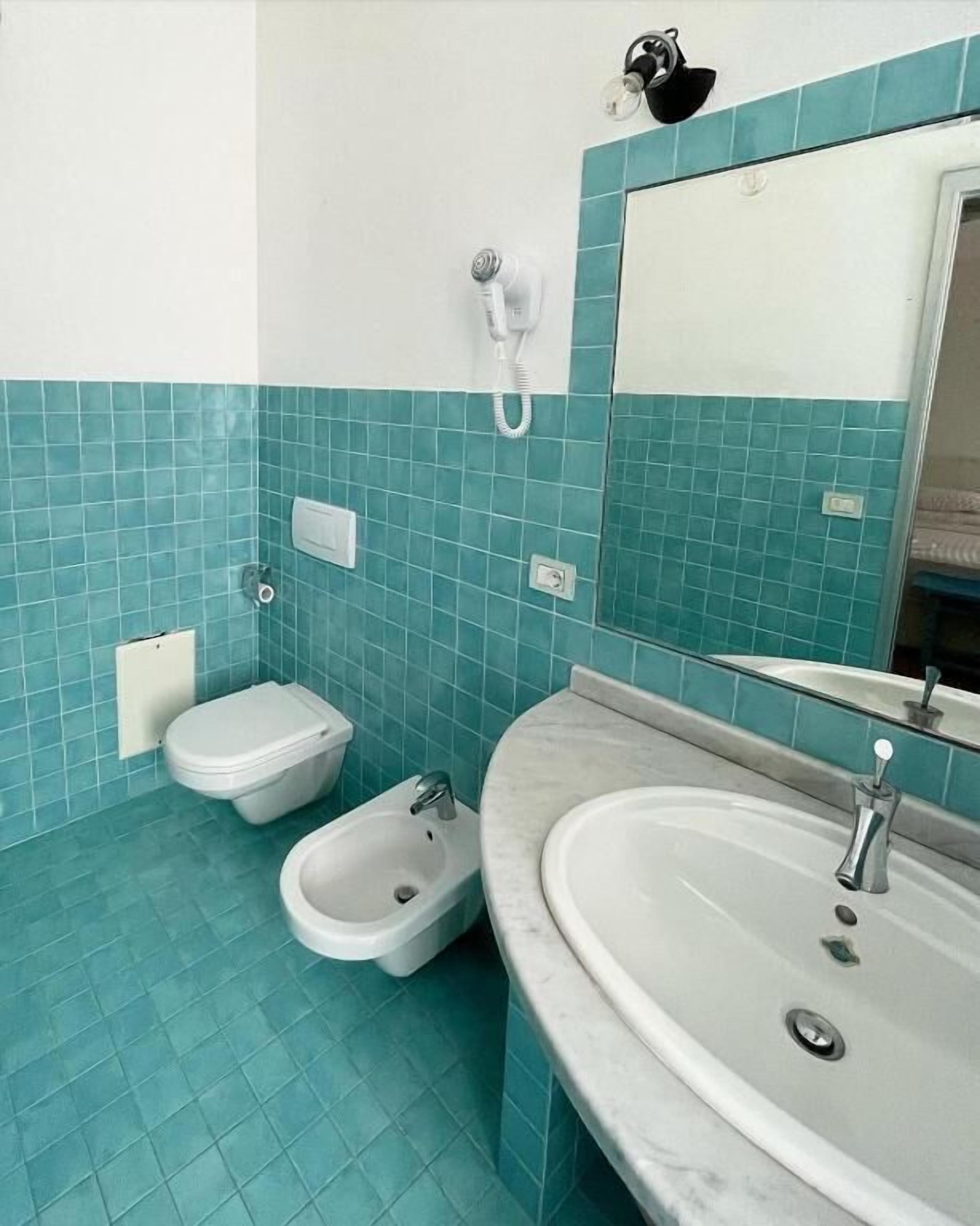 Een badkamer met twee toiletten, een toiletbronsje, een wastafel en een spiegel.