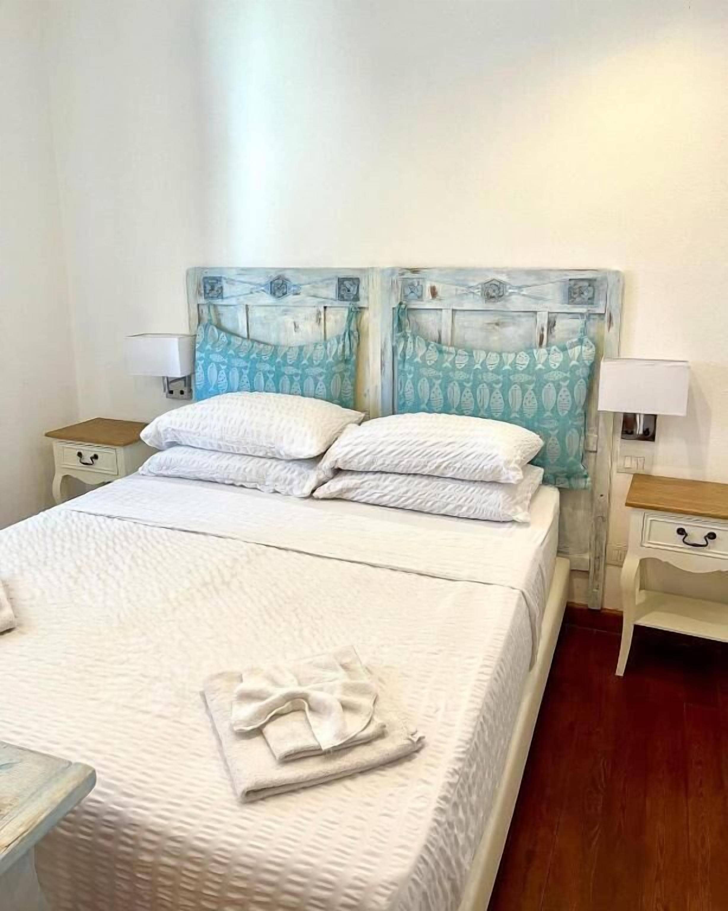 A neatly made bed with white linens and a folded towel, two nightstands with lamps, and a headboard with a fish pattern.