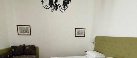 Ein Schlafzimmer mit einem Bett, einem grünen Schlafsofa, einer Chandelüster und zwei gerahmten Bildern an der Wand.
