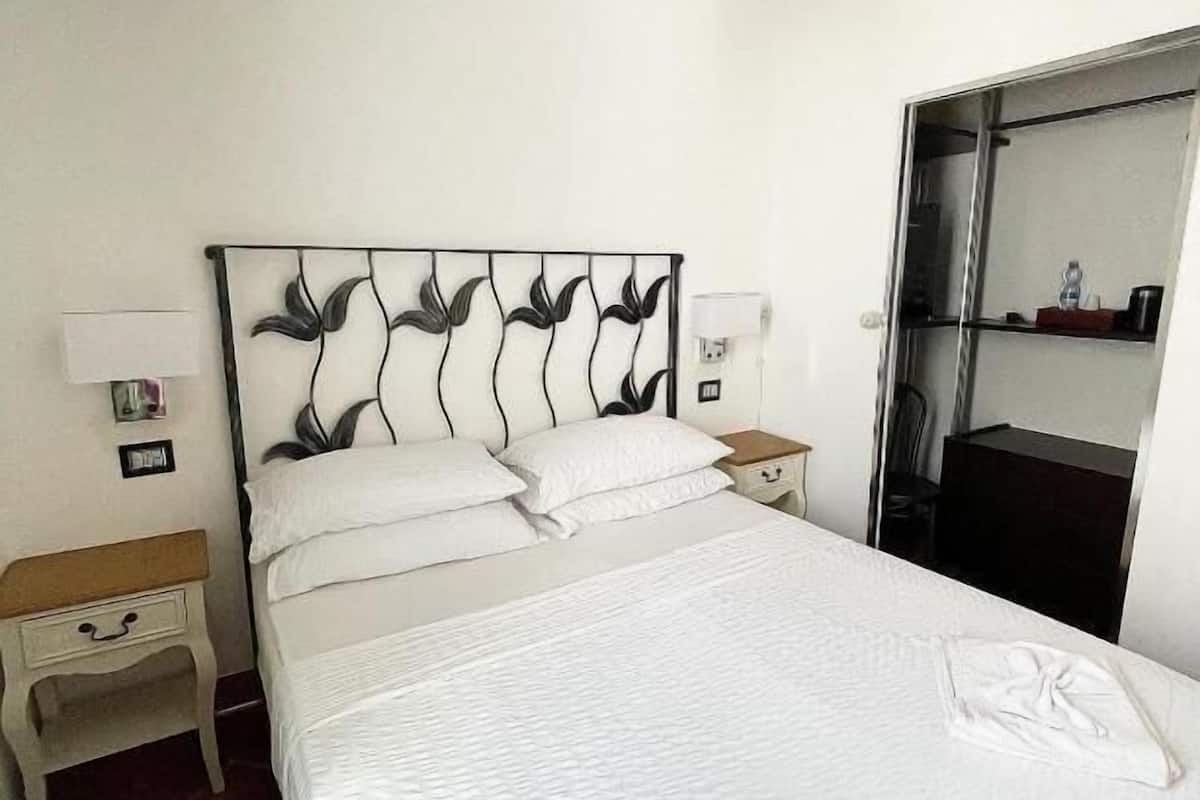 Un lit bien fait, avec du linge de lit blanc et deux oreillers, une table de chevet avec une lampe et un miroir au mur.