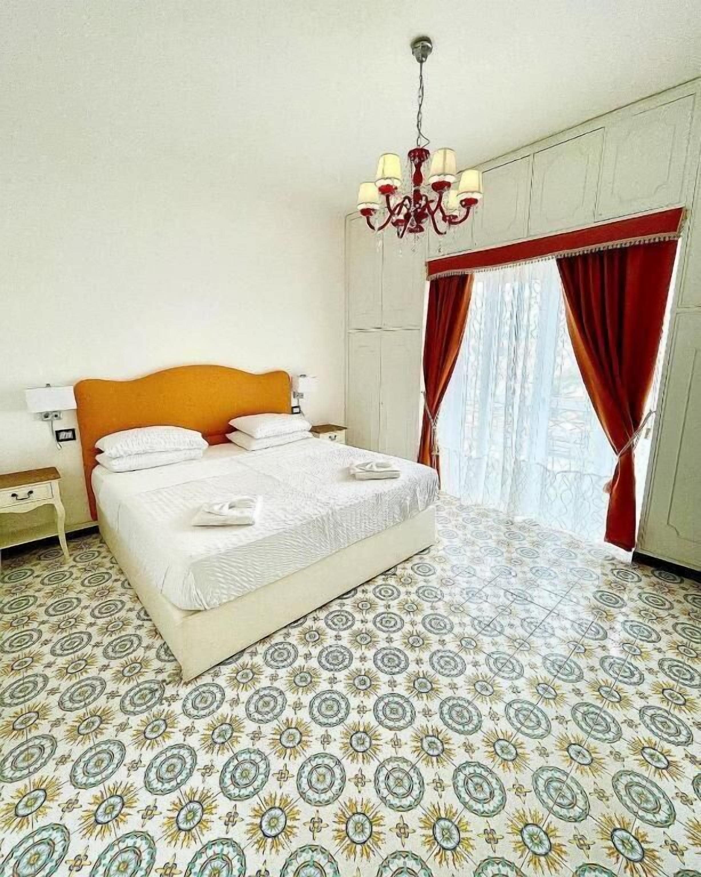 Een slaapkamer met een bed, nachtkastje, een kroonluchter en vloer met een patroon.