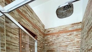 Un espace douche doté d’une porte en verre, d’un pommeau de douche et d’une petite étagère pour les articles de toilette.