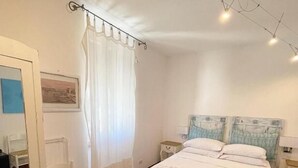 Une chambre à coucher avec un lit, une chaise, une table de chevet, un miroir et un tableau accroché au mur.