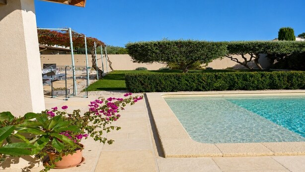 Une piscine à l’eau claire, entourée d’une haie bien entretenue, d’un pot de fleurs et d’une structure en forme de pergola.