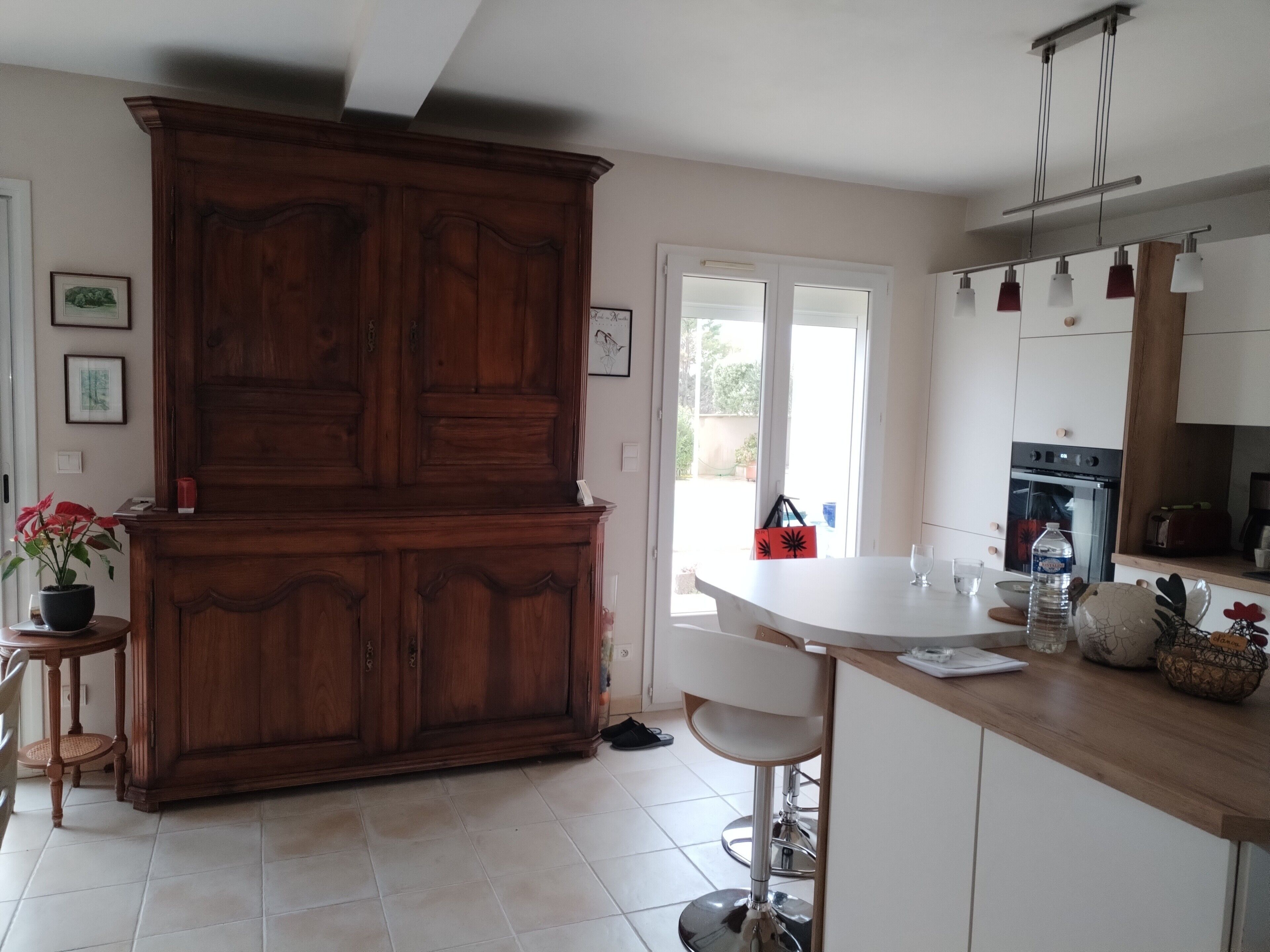 Une cuisine dotée d’un grand meuble en bois, d’un plan de travail blanc et d’un coin repas avec une chaise blanche.