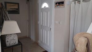 Un couloir avec une porte blanche, un tableau encadré au mur, une lampe sur une table d’appoint et un sac en tissu posé sur le sol.