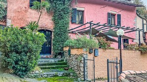 A pink building with a stone staircase leading to a black door, surrounded by greenery and a metal gate. - Stunning  villa for 4 people with TV and terrace (Finale Ligure)