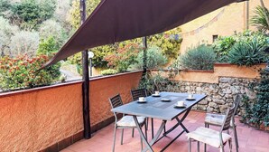 An outdoor patio with a table and chairs, surrounded by a variety of plants and a stone wall. - Stunning  villa for 4 people with TV and terrace (Finale Ligure)